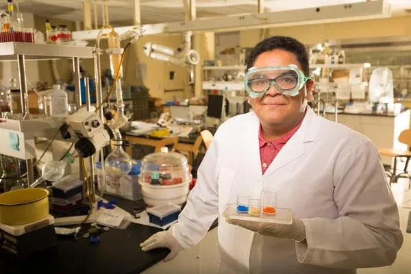 A man in a lab coat holds samples in front of a laboratory